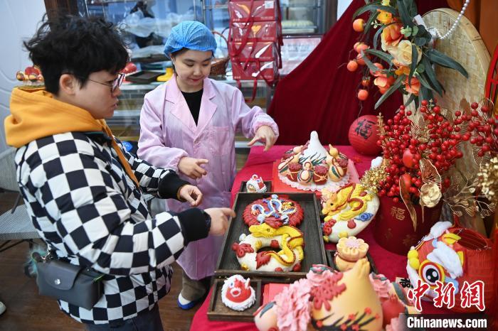1月25日，隨著春節(jié)臨近，蘭州一花饃店“龍”元素花饃熱銷。圖為工作人員向顧客推薦“龍”元素花饃。九美旦增 攝</p><p>